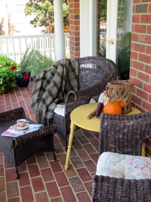 Two brown wicker chairs and a yellow table on a front porch. 