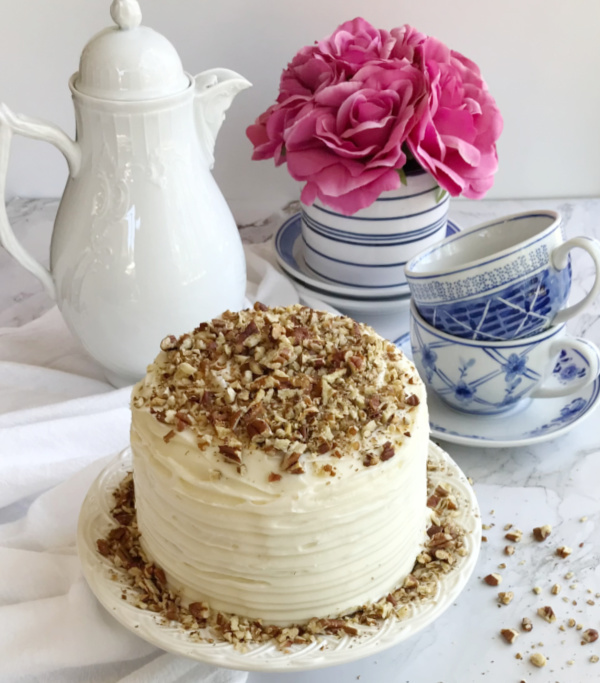Hummingbird cupcakes cake with 2 blue and white tea cups a blue and white vase of pink roses and a white teapot.