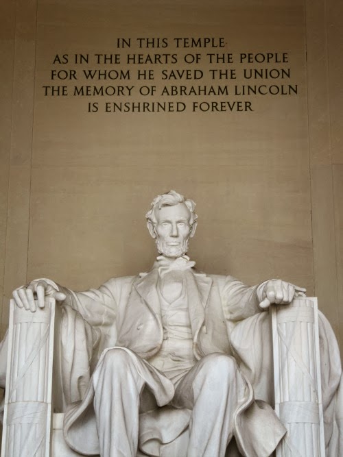Statue of Abraham Lincoln at the Lincoln Memorial, Lincoln is sitting in a chair and behind him carved in the wall "In this temple as in the hearts of the people for whom he saved the union the memory of Abraham Lincoln is enshrined forever. 