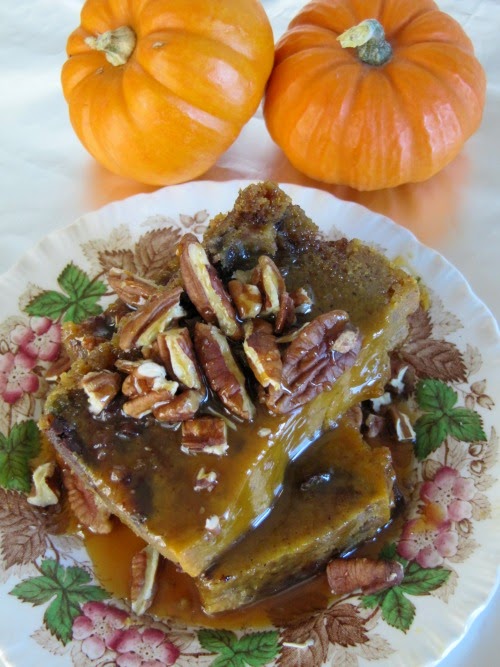 Pumpkin Bread Pudding with Salted Caramel Sauce and Toasted Pecans on a brown, red and white transfer ware plate with 2 orange pumpkins sitting next to it.