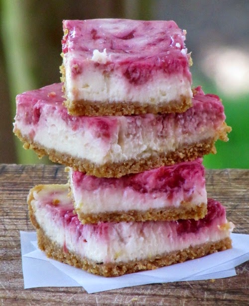 Four Lemon Raspberry Swirled Cheesecake Bars stacked on a wood cutting board. 
