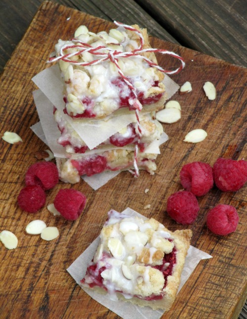 raspberry-almond-shortbread-bars in a stack tied with red and white twine on a wood board with scattered raspberries.