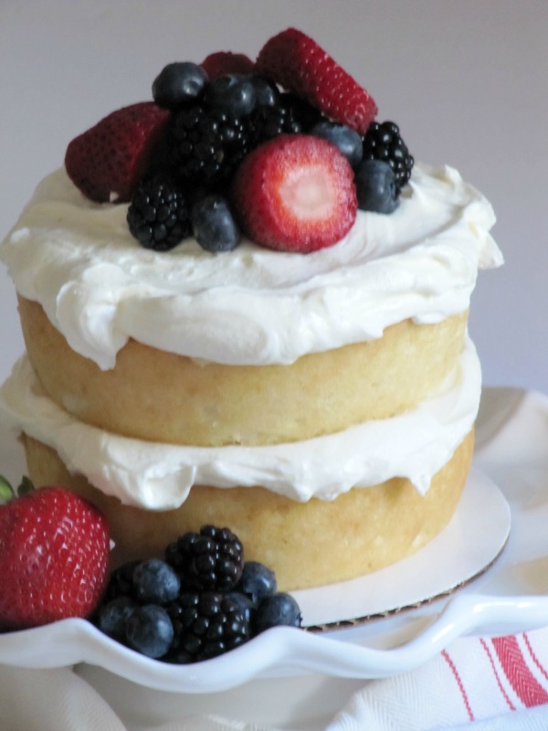 White cake with white frosting with strawberries and blueberries piled on top. 