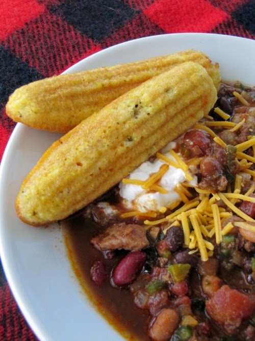 chili in a white bowl with cheese, sour cream and 2 corn bread sticks.