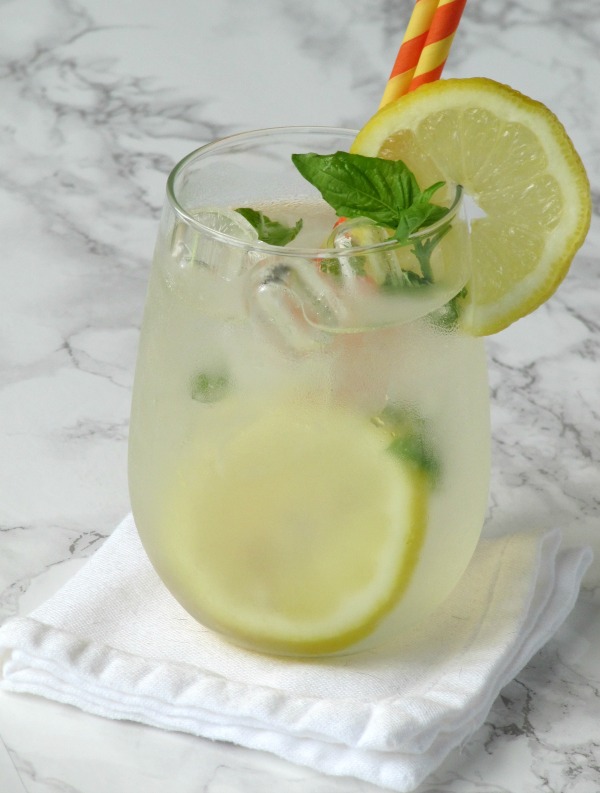 a clear glass filled with lemonade, lemons and a sprig of basil.