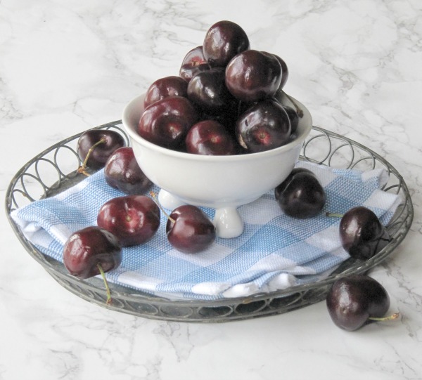cherries in a white bowl sitting on a gingham napkin. 