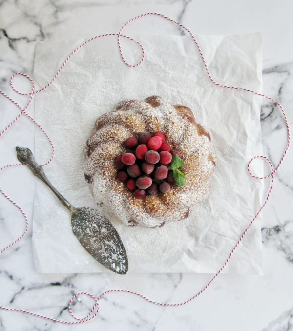 cranberry bundt cake on a marble slab with a silver-plate cake server on the left. 
