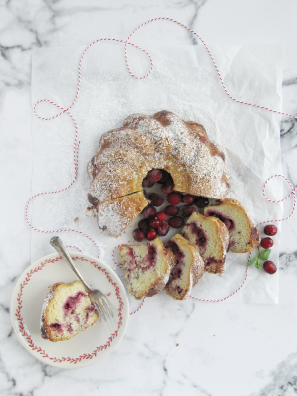 sliced cranberry bundt cake on a marble slab with one piece on a plate.