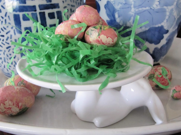 white cake plate with a rabbit holding grass and colorful easter eggs