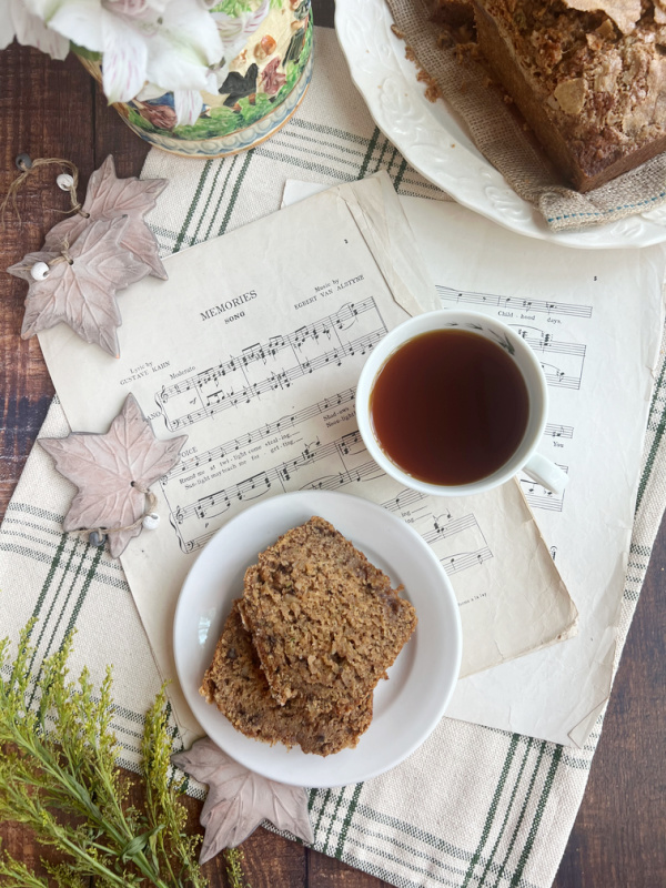 pumpkin zucchini bread sliced on a plate with a cup of tea, sheet music and flowers.