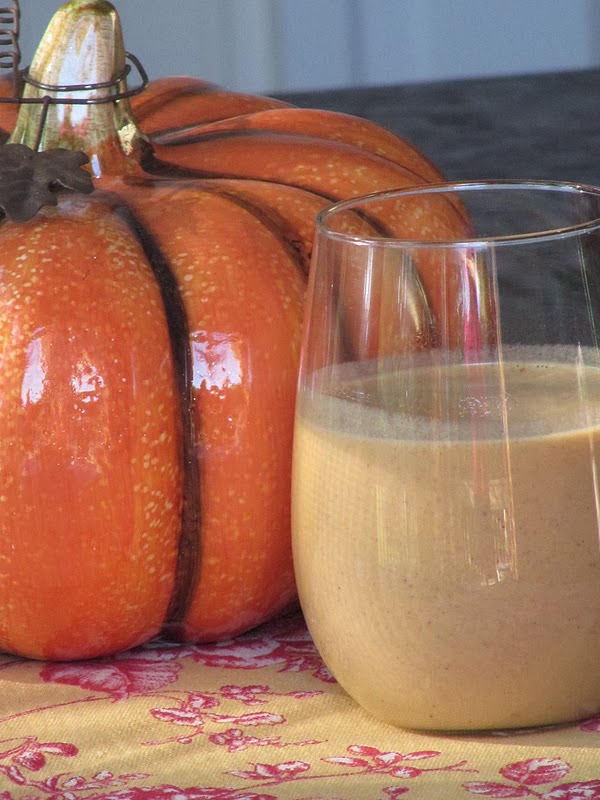 pumpkin white hot chocolate in a glass with a orange ceramic pumpkin
