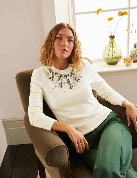 woman sitting in a chair wearing a white sweater embellished with crystals