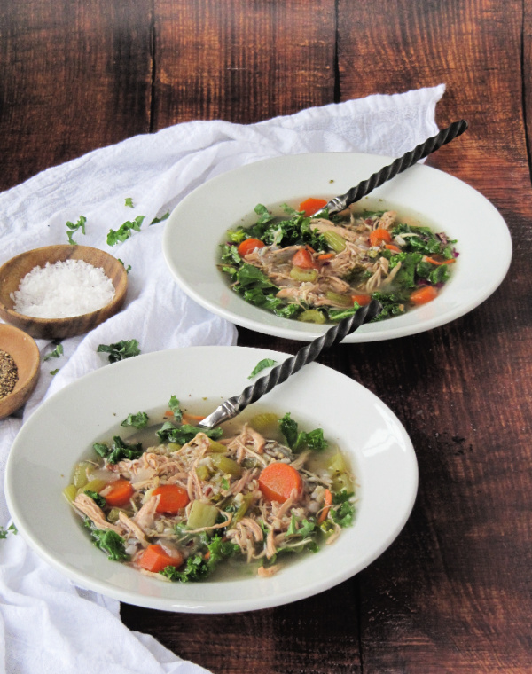 Chicken wild rice soup with kale in white bowls on a wood background