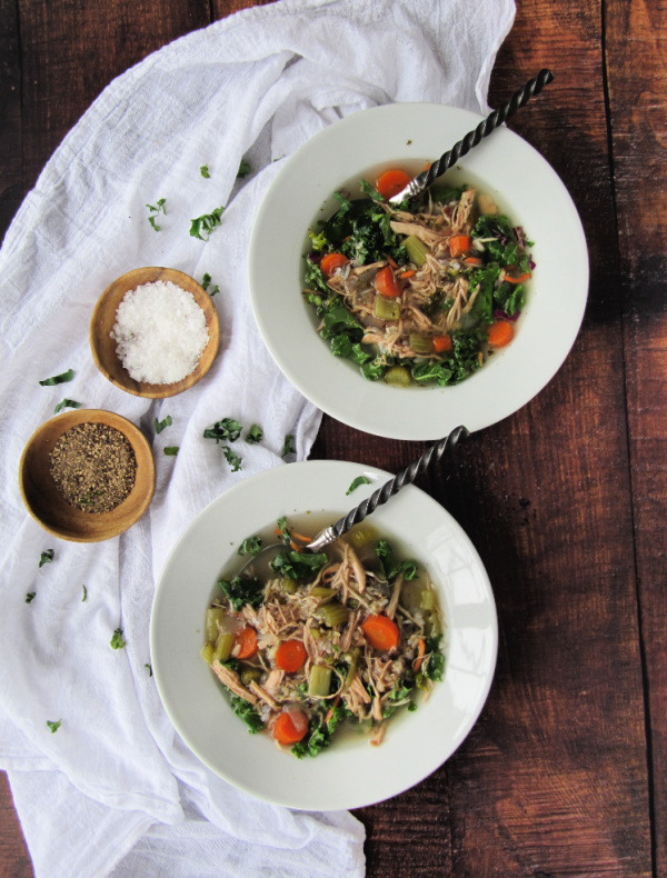 chicken wild rice soup with kale in white bowls with salt and pepper on wood background
