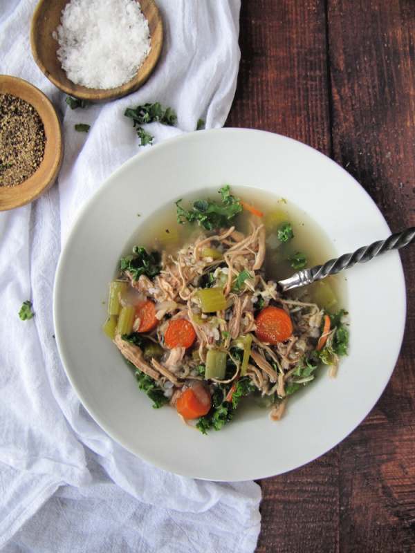 chicken wild rice soup with kale in white bowls and with salt and pepper in small bowls