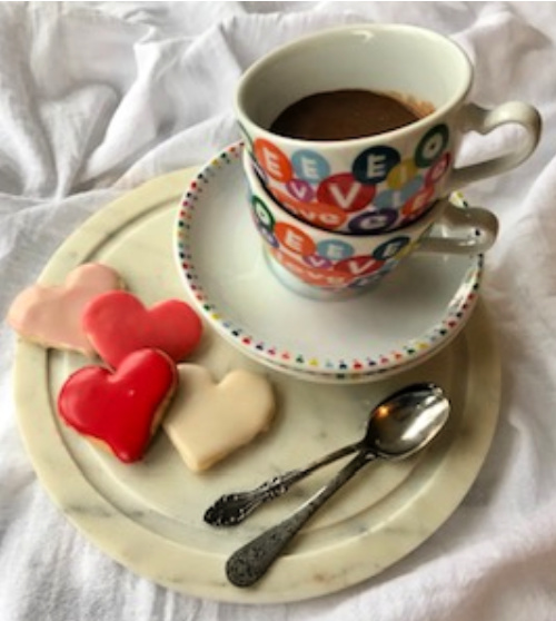 Two cups with heart patterns sitting on a marble circle and heart shaped sugar cookies.