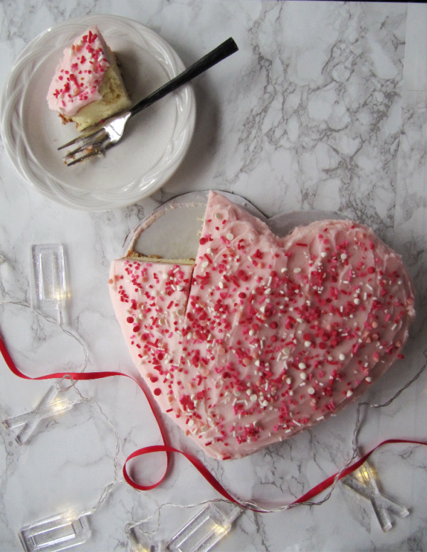 Heart shaped cake with a piece cut out on a plate in the top left corner.
