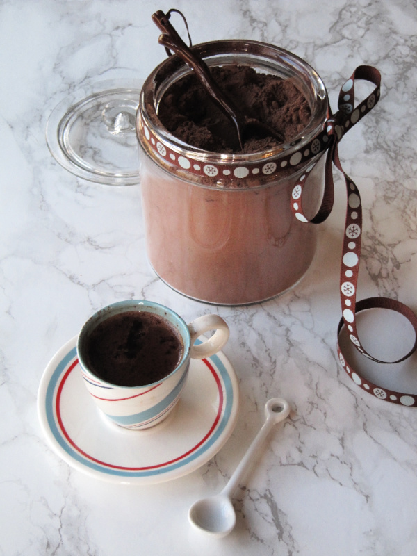 Homemade hot cocoa mix in a glass container with a cup beside it