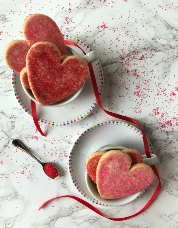two cups on saucers filled with heart shaped cookies 
