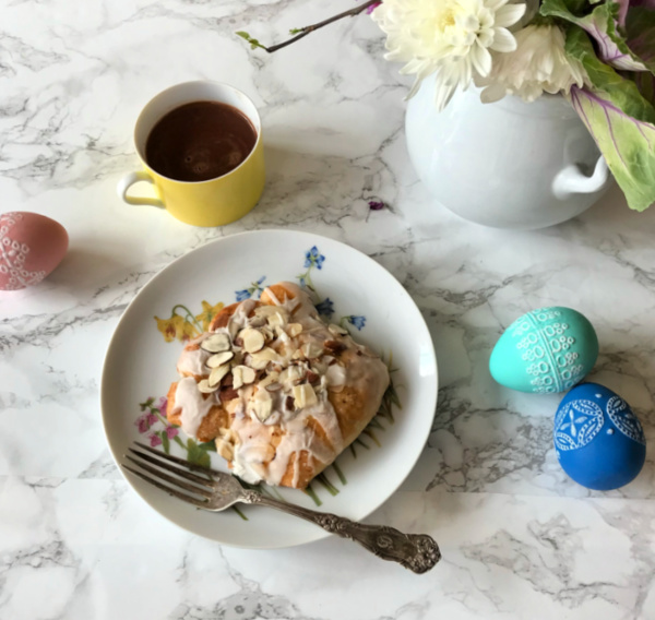 Bear Claw pastry on a flower plate with a yellow cup filled with hot chocolate and a vase of flowers