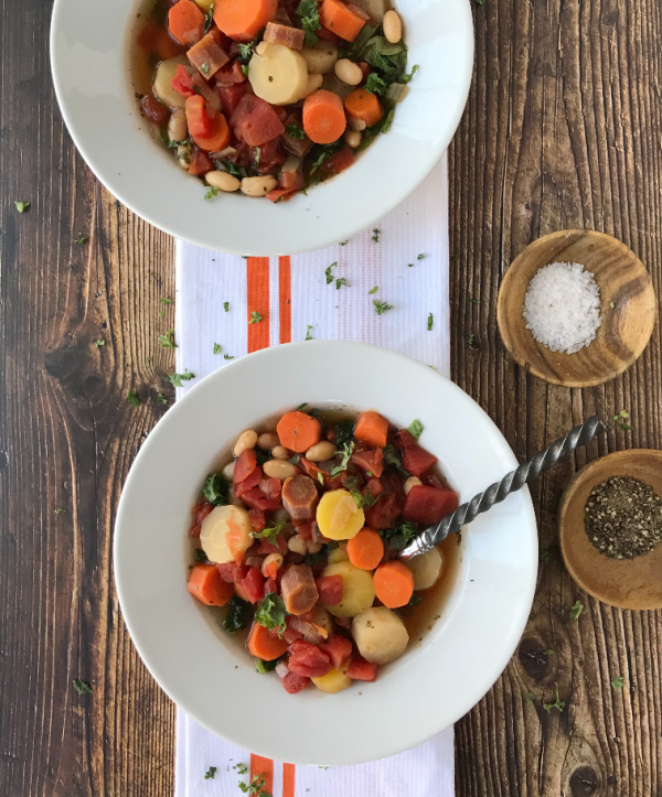 Tuscan carrot soup in white bowls on a white towel with orange stripe and a wood background