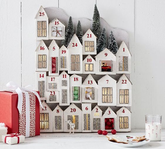 Light Up Glitter Houses Advent Calendar witting on a table with a candle and Christmas ribbon nearby