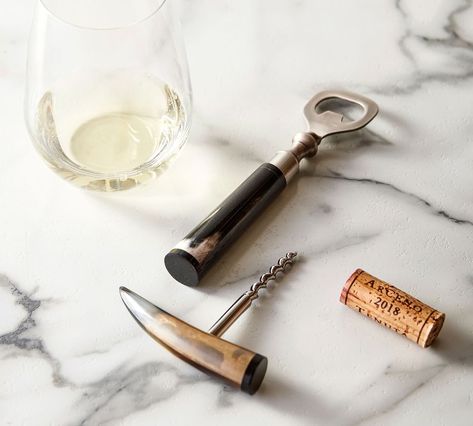 a glass of white wine with a grin bottle opener and a horn wine opener on a marble background