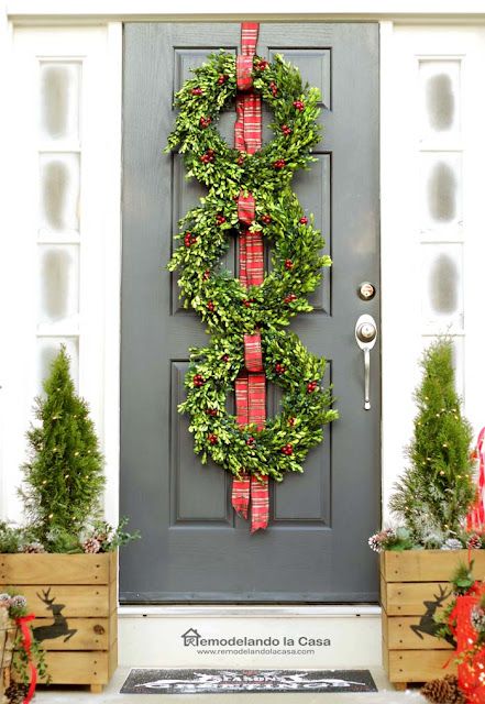 three Christmas Wreaths on a black door with two small trees in posts next to it, front door decorations for christmas. 