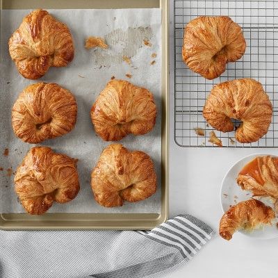 A silver pain with 5 croissants next to a baking rack with three croissants and a blue striped towel 