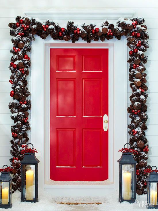 Red door on a White House with a pinecone garland around the door and lanterns on the front
