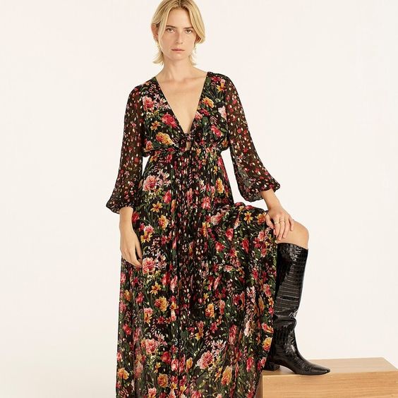 Woman wearing a black dress with flowers and her booted foot up on a table