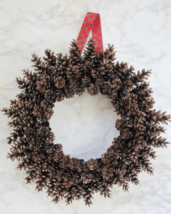 Pinecone wreath with plaid ribbon hanger on a marble backround
