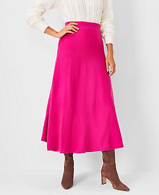 Image of the lower half of a woman in a white sweater and fuchsia pink skirt with brown boots standing with her hand on hip