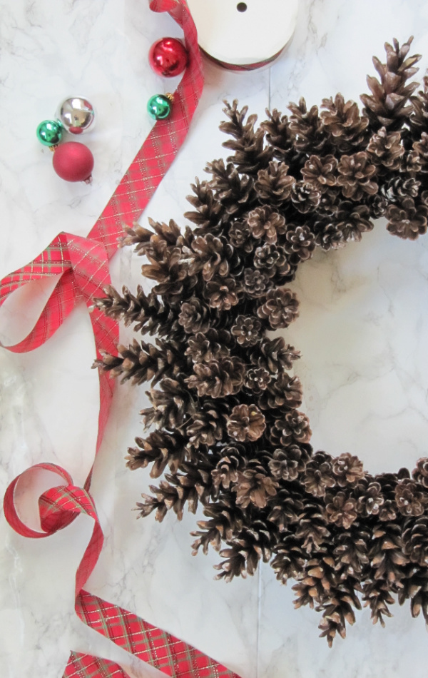 pinecone wreath and some plaid ribbon with red and green christmas ornaments