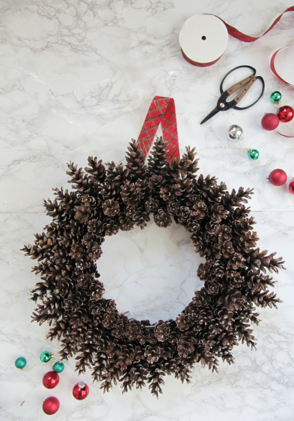 pinecone wreath on wire frame no glue with tartan ribbon scissors and green and red christmas ornaments