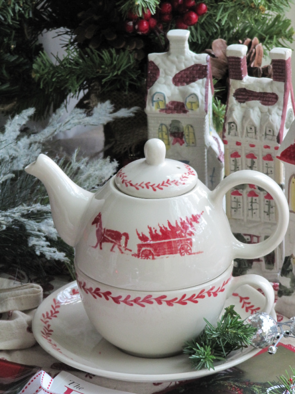 Red and White Williamsburg Teapot sitting in front of two porcelain houses and christmas foliage