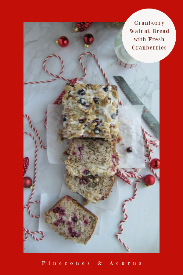 cranberry walnut loaf wrapped in white paper and tied with red and white string on a white piece of marble with scattered christmas bulbs a snow globe and string