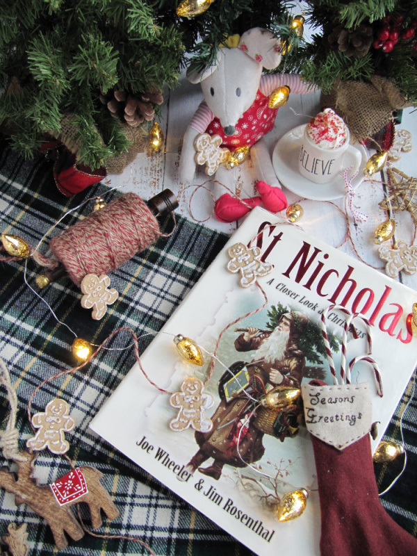 flatly of St.Nicholas books and a small bonus with a cup of hot chocolate on a green plaid background with gingerbread men and christmas lights.