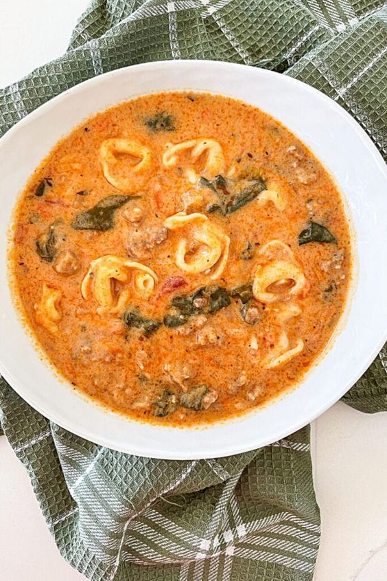 white bowl filled Italian Tortellini Soup. sitting on a green napkin