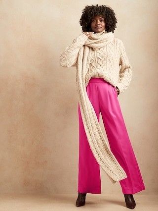 Black model wearing a white sweater and scarf with a pair of fuchsia pink pants and black boots