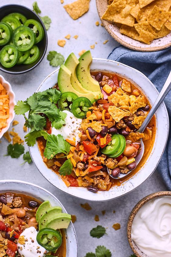 Taco Soup in a white bowl with small bowls of cheese, sour cream, and jalapeño peppers