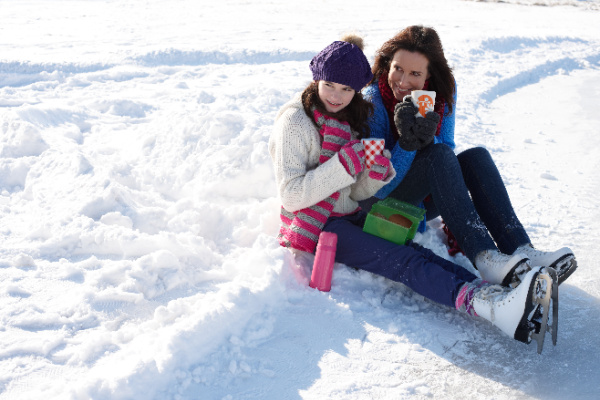 Mother and daughter sitting in snow with ice skates on sitting in the snow