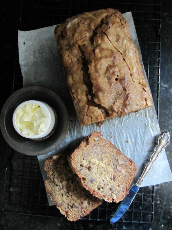 overhead shot of a loaf of banana bread with two slices a knife and small ramekin of butter