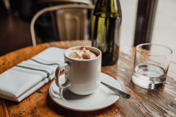 cup of hot chocolate and a glass of water on a table with a green bottle filled with water