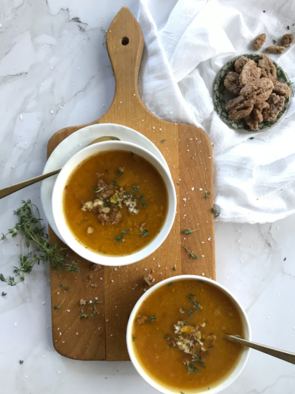 easy roasted butternut squash pumpkin soup in white bowls sitting on a brown cutting board with a white cloth in the right hand corner and a small bowl of pecans