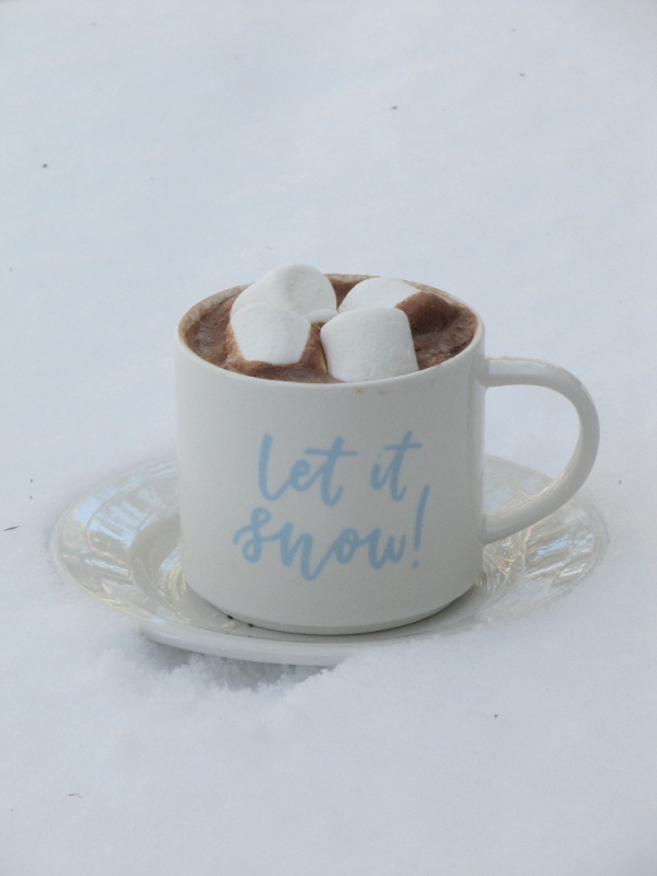hot chocolate and marshmallows in a let it snow mug on a snow topped table