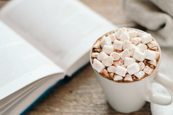 open book and a white mug of hot chocolate with lots of marshmallows