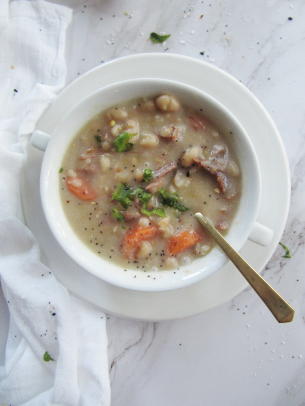 slow cooker ham and bean soup in a white bowl with a spoon and a white napkin on left side