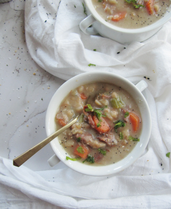 two white bowls with handles filled with ham and bean soup with carrots on has a gold spoon