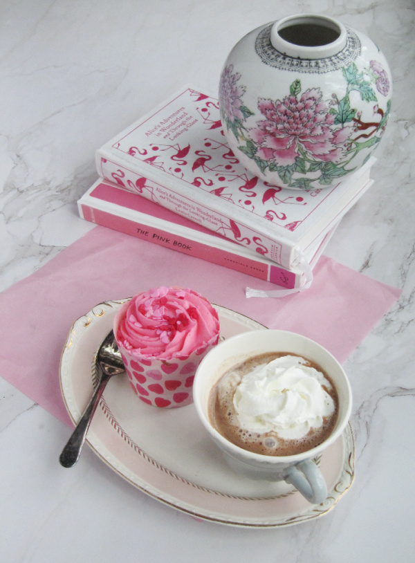 pink cupcake with a cup of hot chocolate and two books